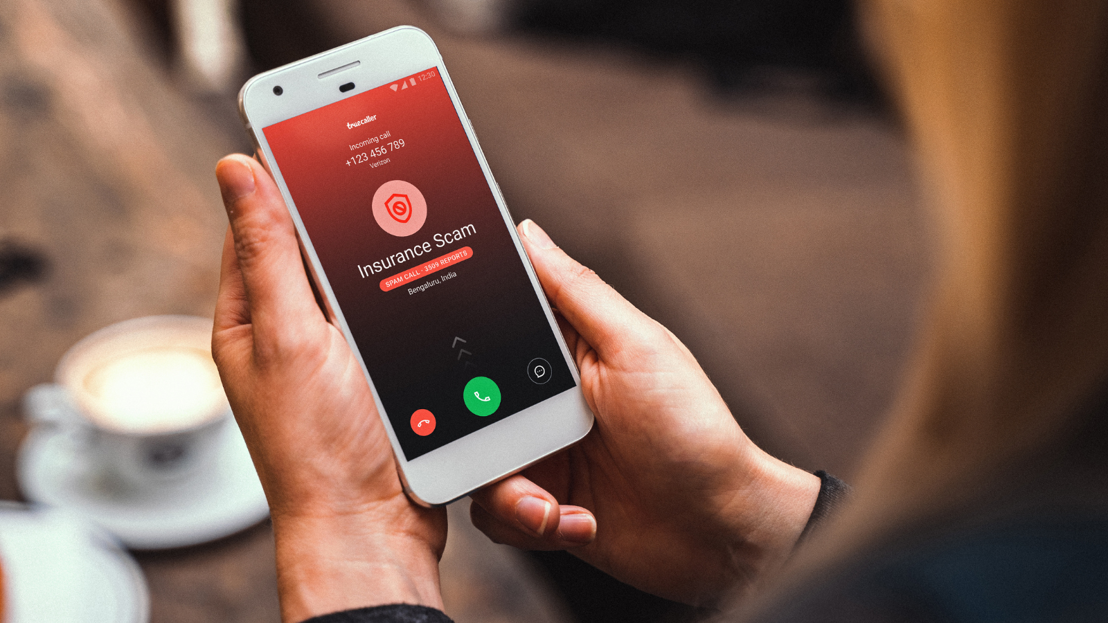a woman holding an iphone receiving a call that's flagged as spam by the truecaller app
