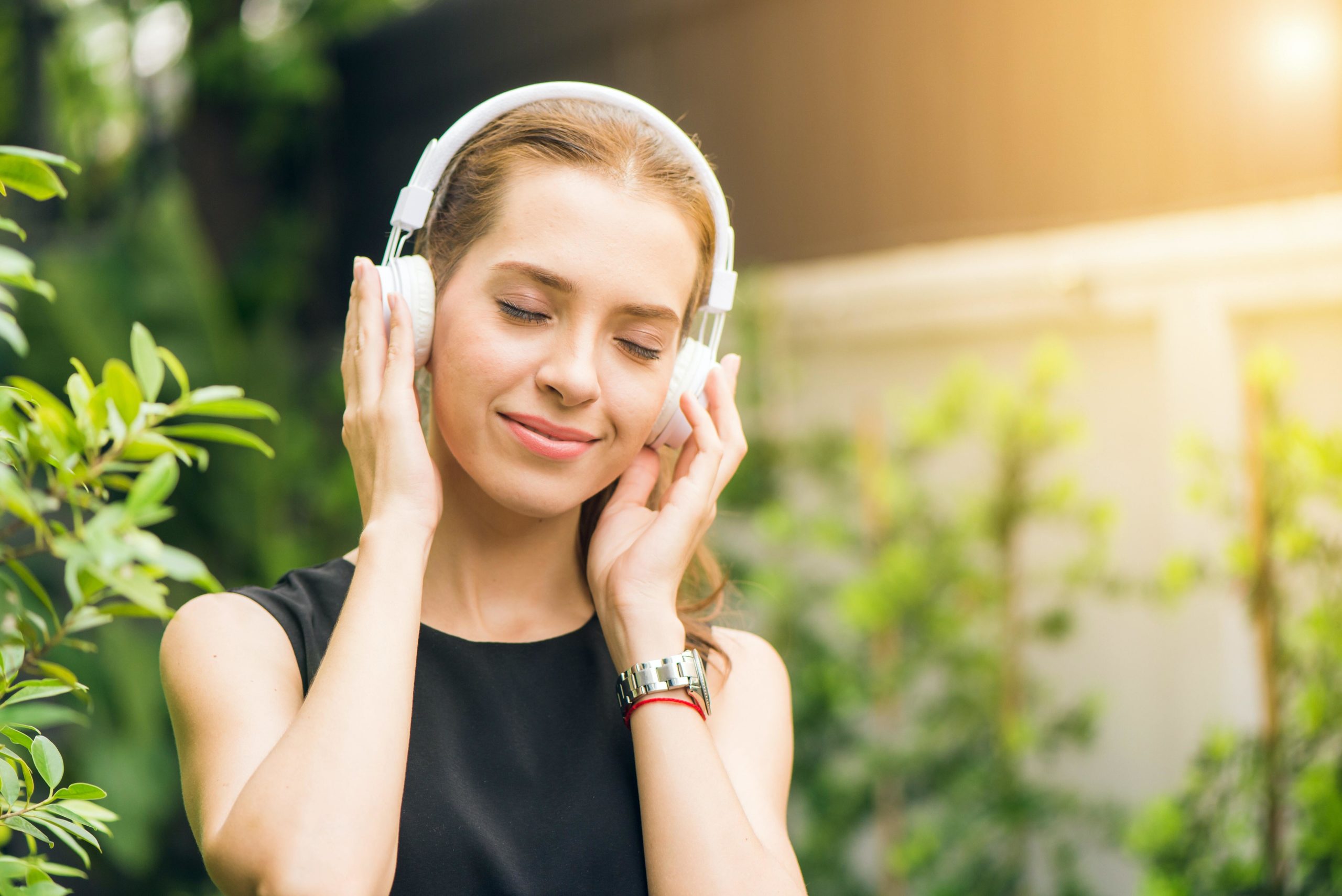 A woman wearing headphones standing outside in greenery.