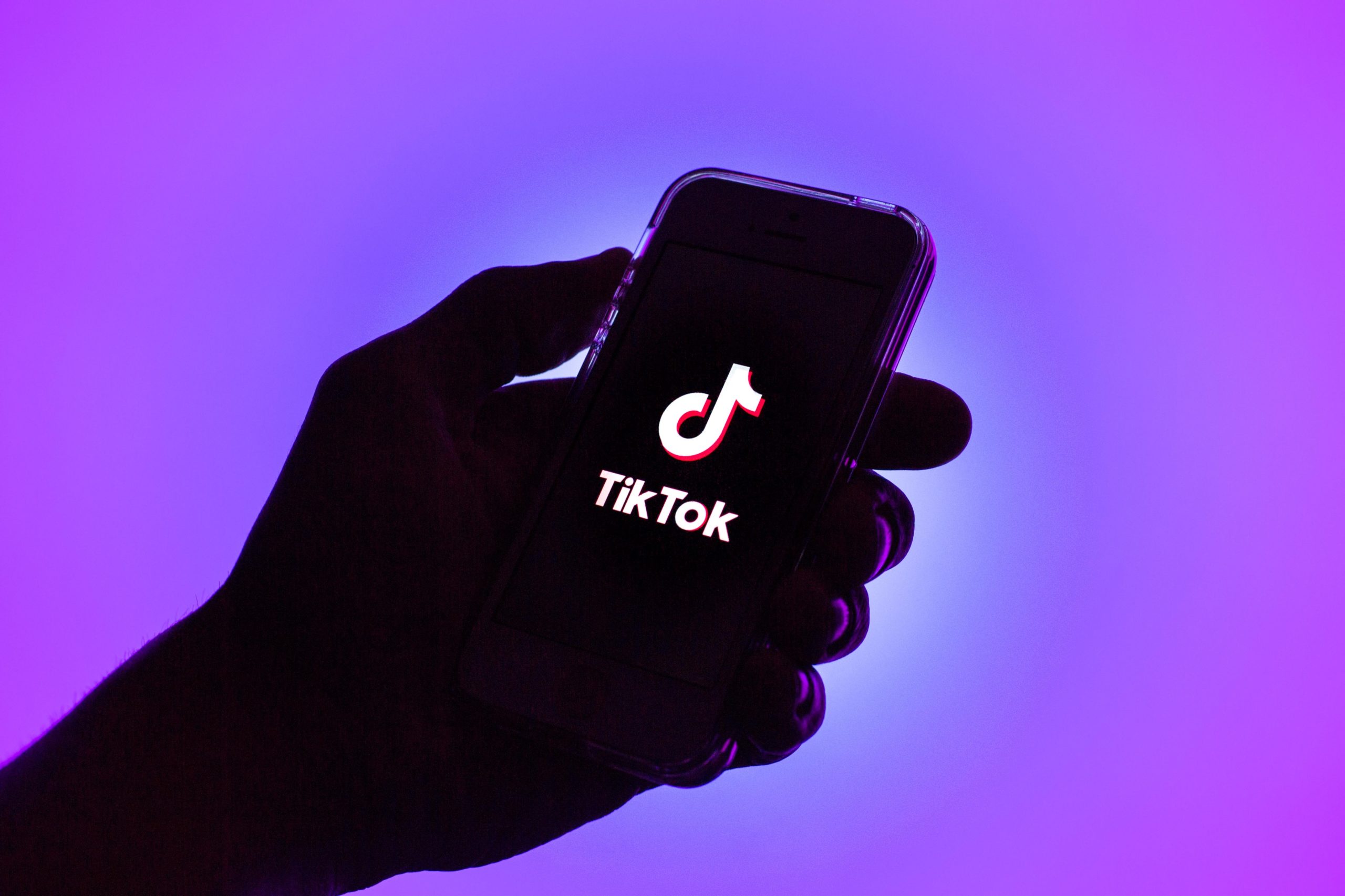 Hand holding a phone with the TikTok logo with a purple background.