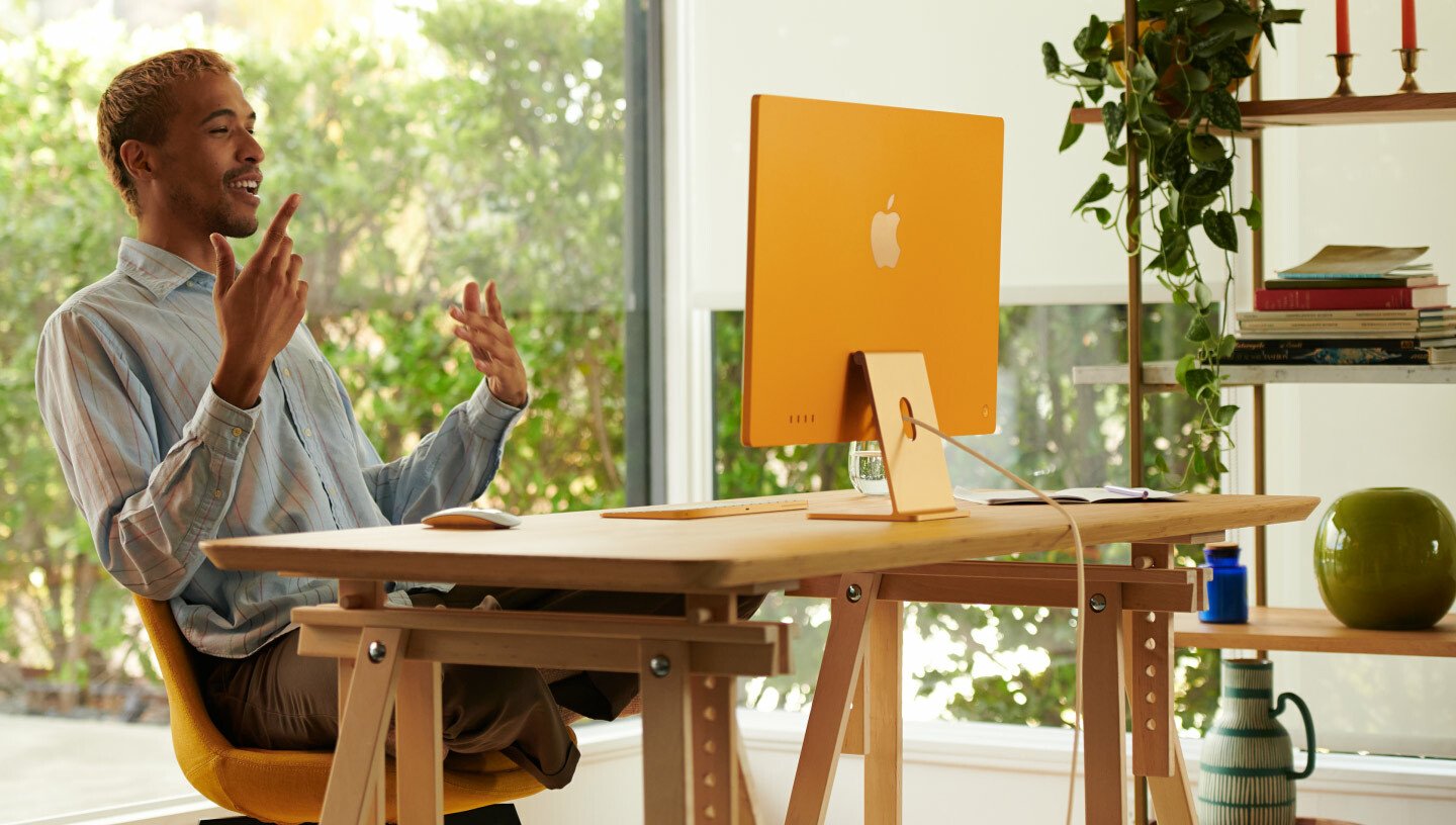 Mac sitting at desk working on yellow Apple iMac 24-inch computer