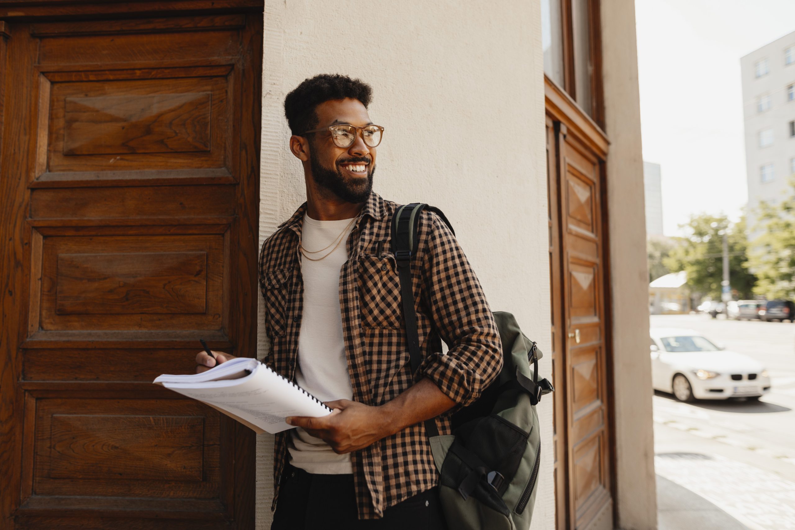Male college student entering doorway of college. with papers in hand and carrying backpack