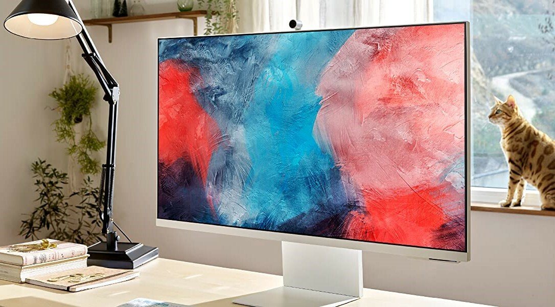 Samsung M80B 32-inch smart computer monitor on a desk with a lamp and cat on windowsill behind it