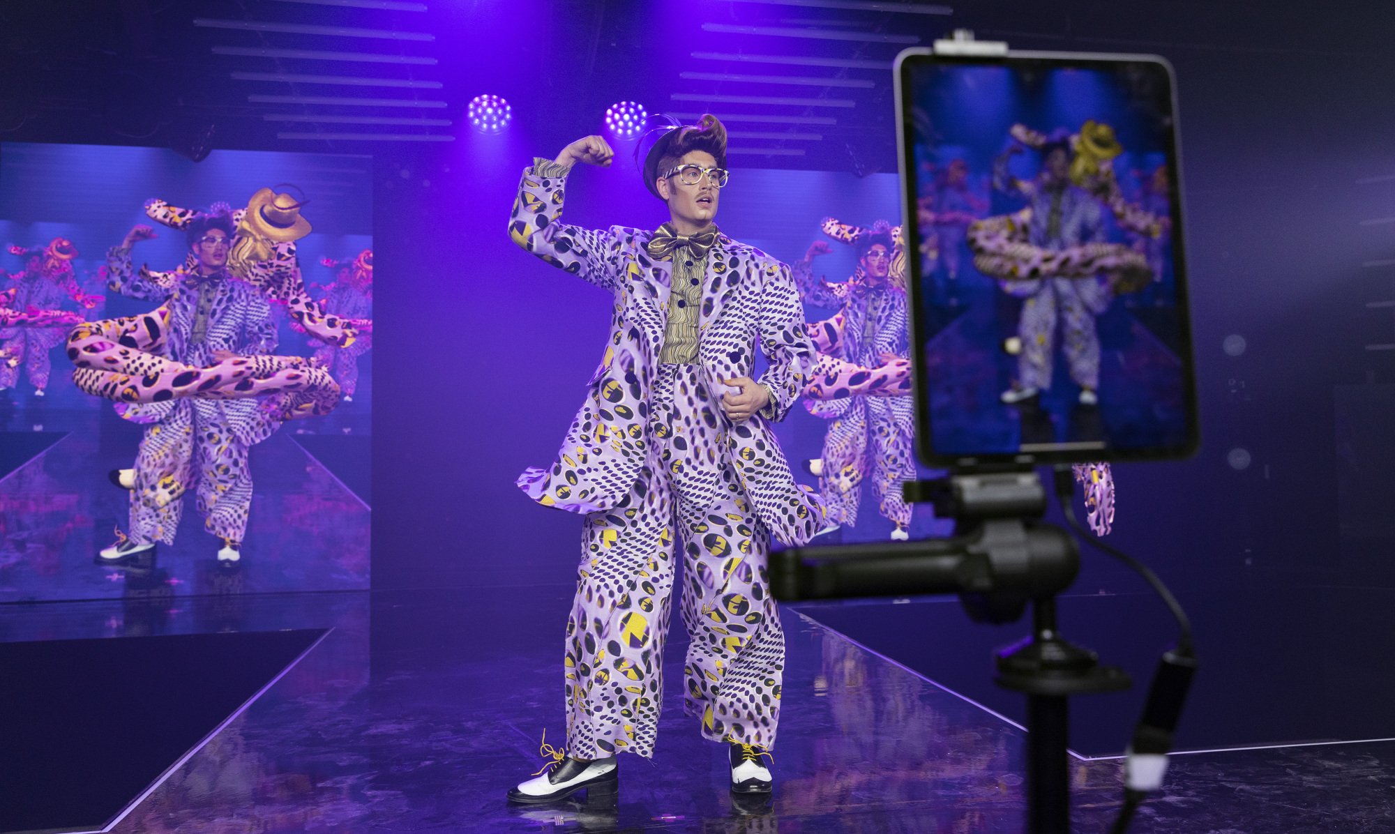 An image of Adam All on stage, with a phone screen displaying the digital fashion outfit in front of it.
