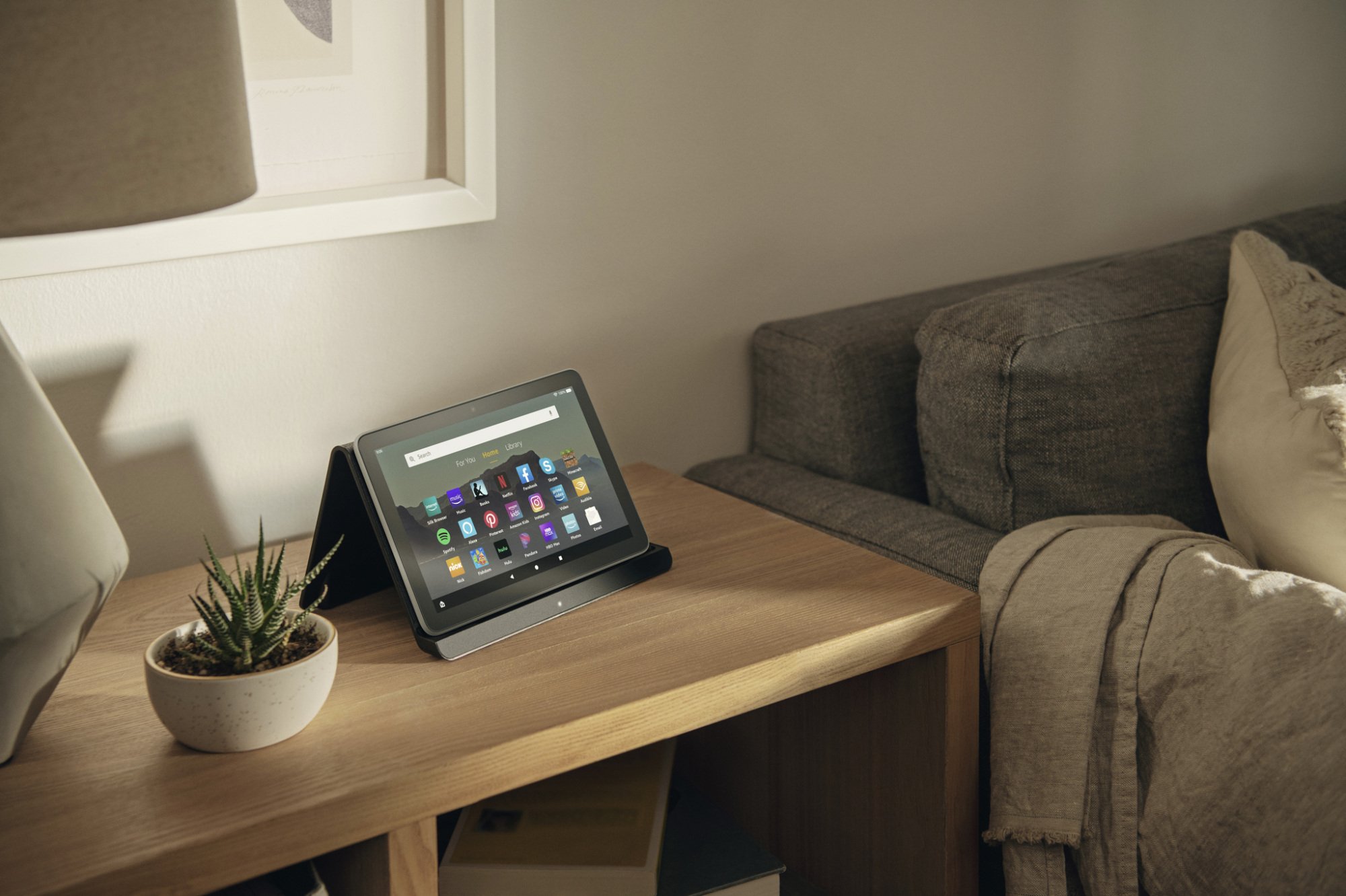 the fire hd 8 plus propped up on its wireless charging dock on a wooden table next to a couch