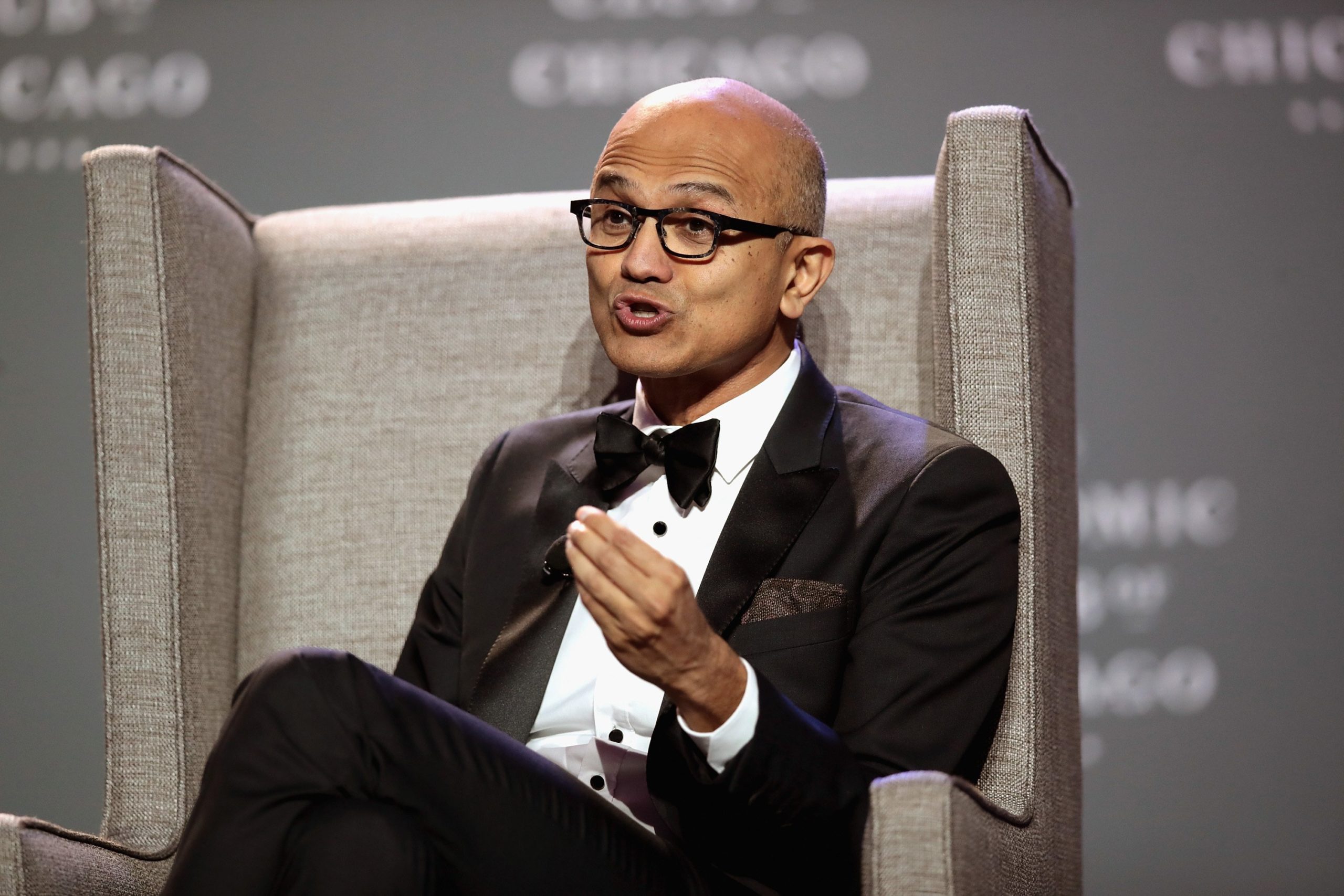 Microsoft CEO Satya Nadella speaking in a black tail coat with bowtie while he sits in a chair.