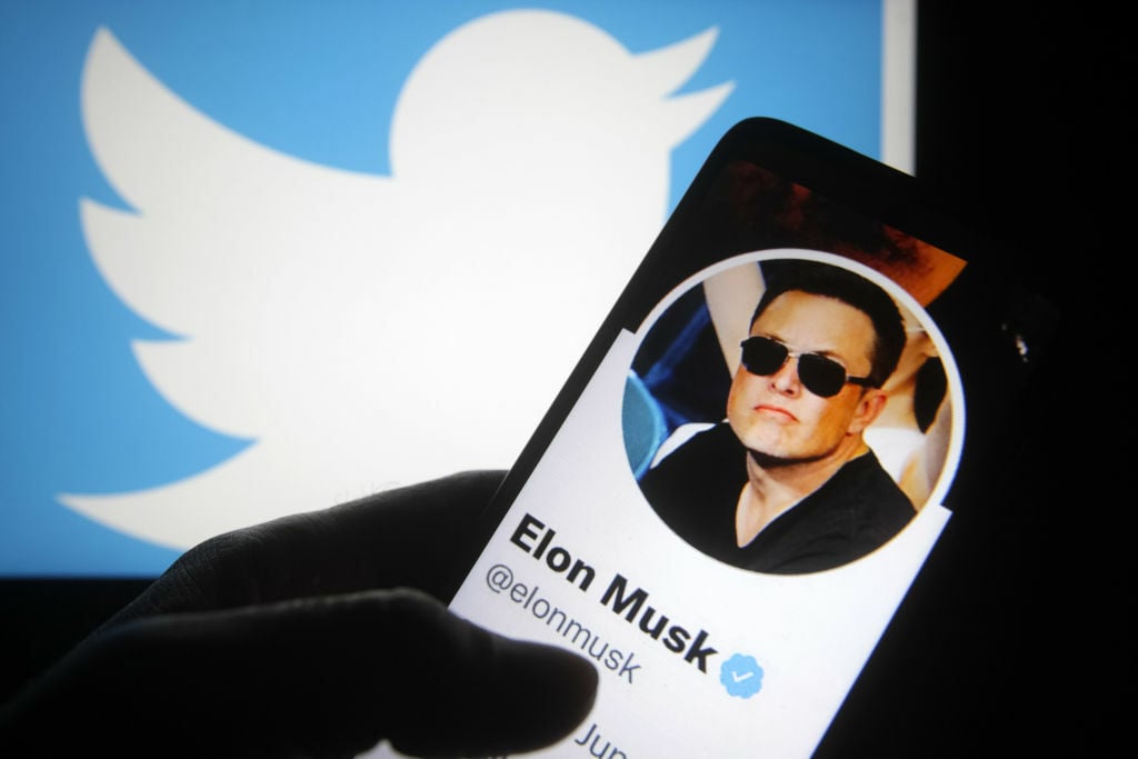 Elon Musk's twitter account on a smartphone, in front of the Twitter logo.