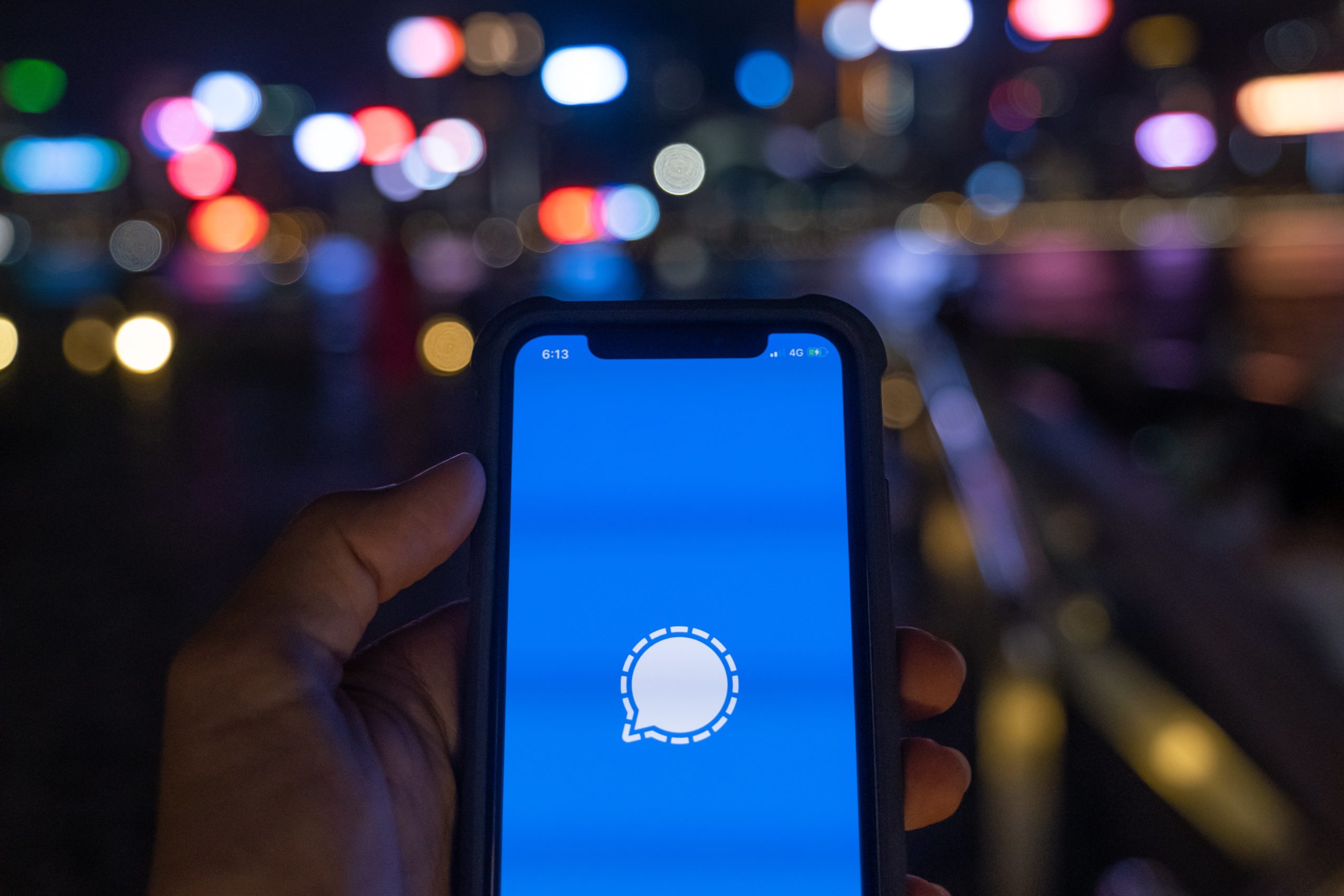 A phone is held out in front of a night time skyline. On the screen is the blue and white Signal icon.