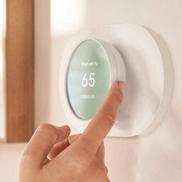 Person using Google Nest Thermostat on wall.