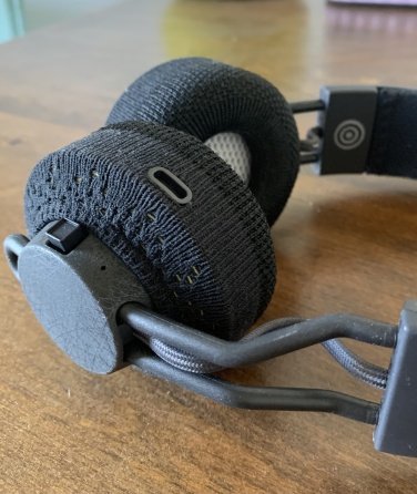 A photo of the right side of the headphones, where a charging port and raised square button are visible along the earpiece.