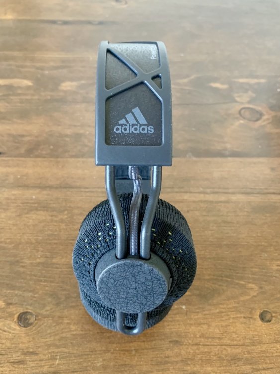 The side of the headphones, against a wooden background. You can see part of the band, which is printed with the Adidas logo, and the earpiece.