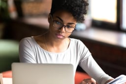 Thoughtful millennial woman in glasses looks at laptop screen