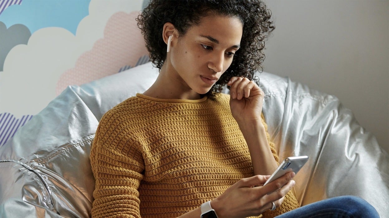 A woman is using her Apple AirPods 2nd Gen which she has connected to her smartphone