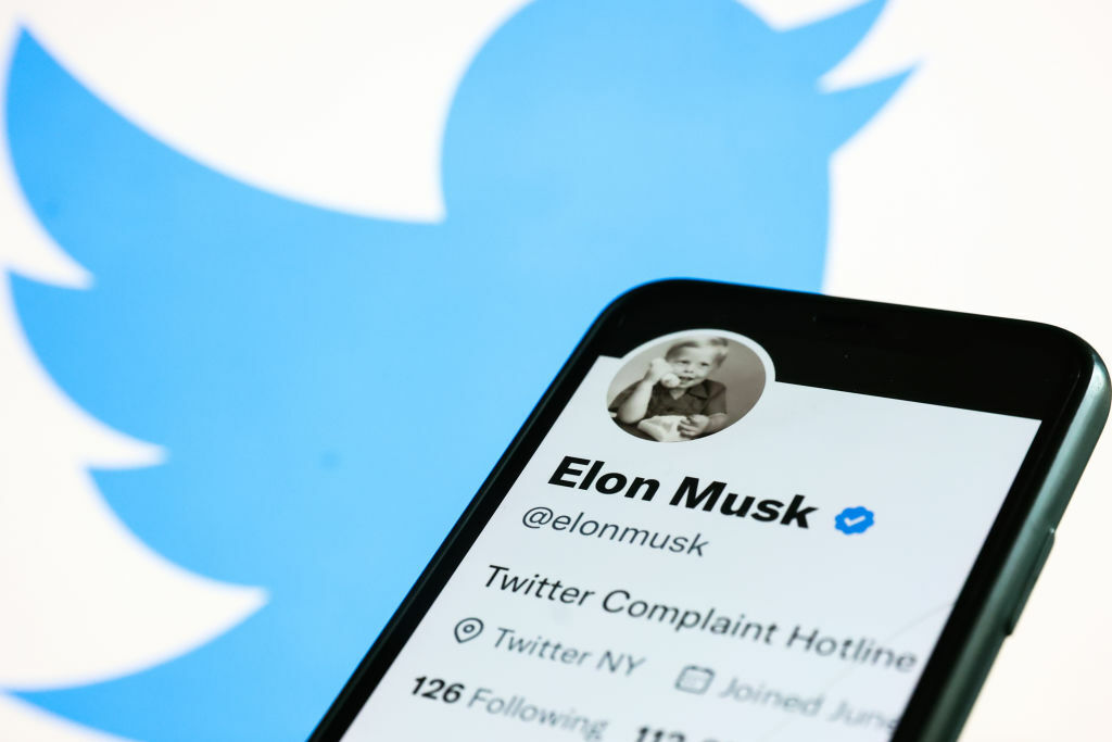Elon Musk's Twitter account on a smartphone, held in front of the Twitter logo.