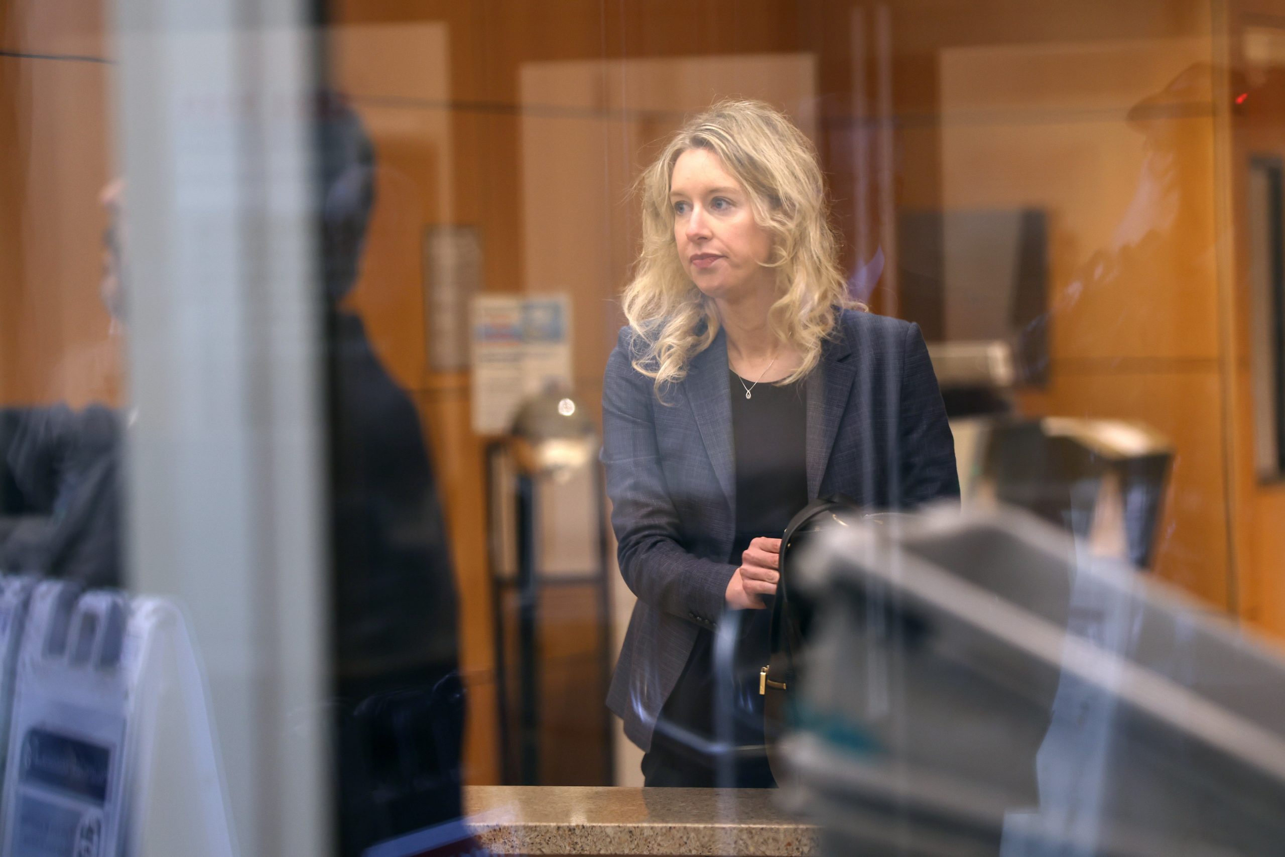 A blonde woman is seen through a see-through glass panel in a court building.