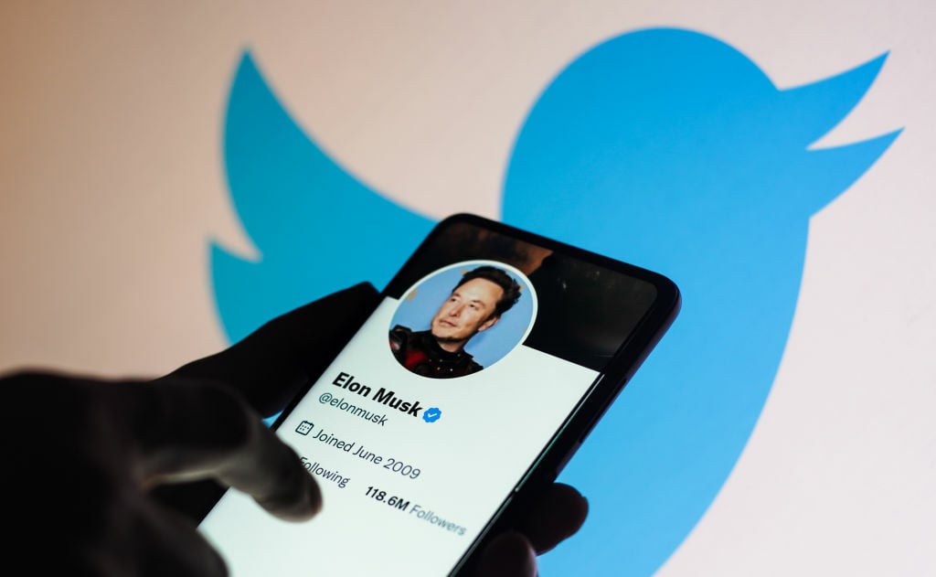 Elon Musk's Twitter account on a smartphone, in front of the Twitter logo.