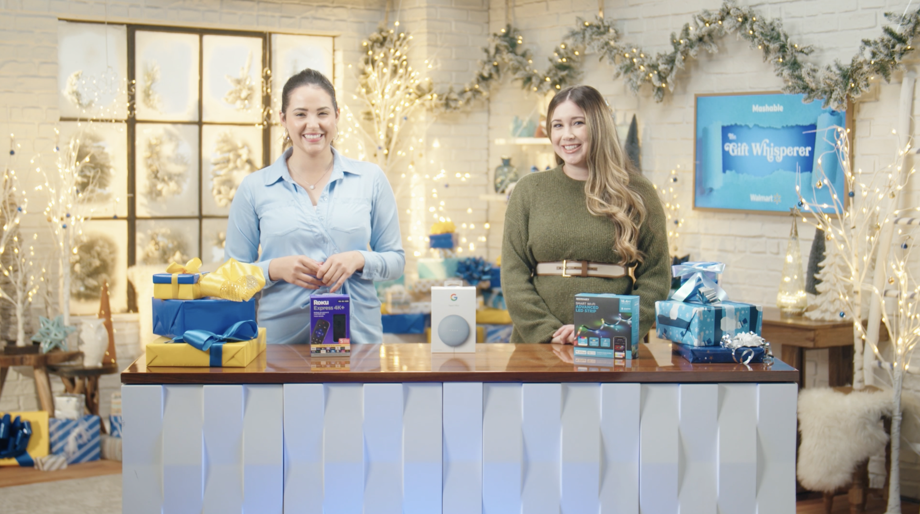 Cathy Pedrayes and Gaby from Mashable standing in a room decked with holiday decor, three products in front of them.