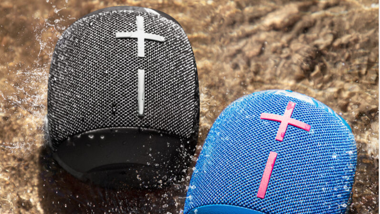 Black bluetooth speaker on the left, blue one on the right on top of a rocky background.