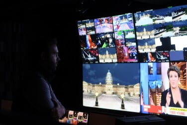 The side profile of a man is lit by screens in a pitch black room.