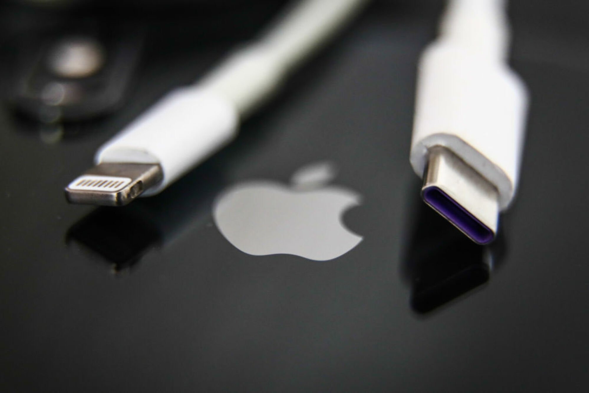 a lightning cable and USB-C cable on top of an iPhone showing the Apple logo