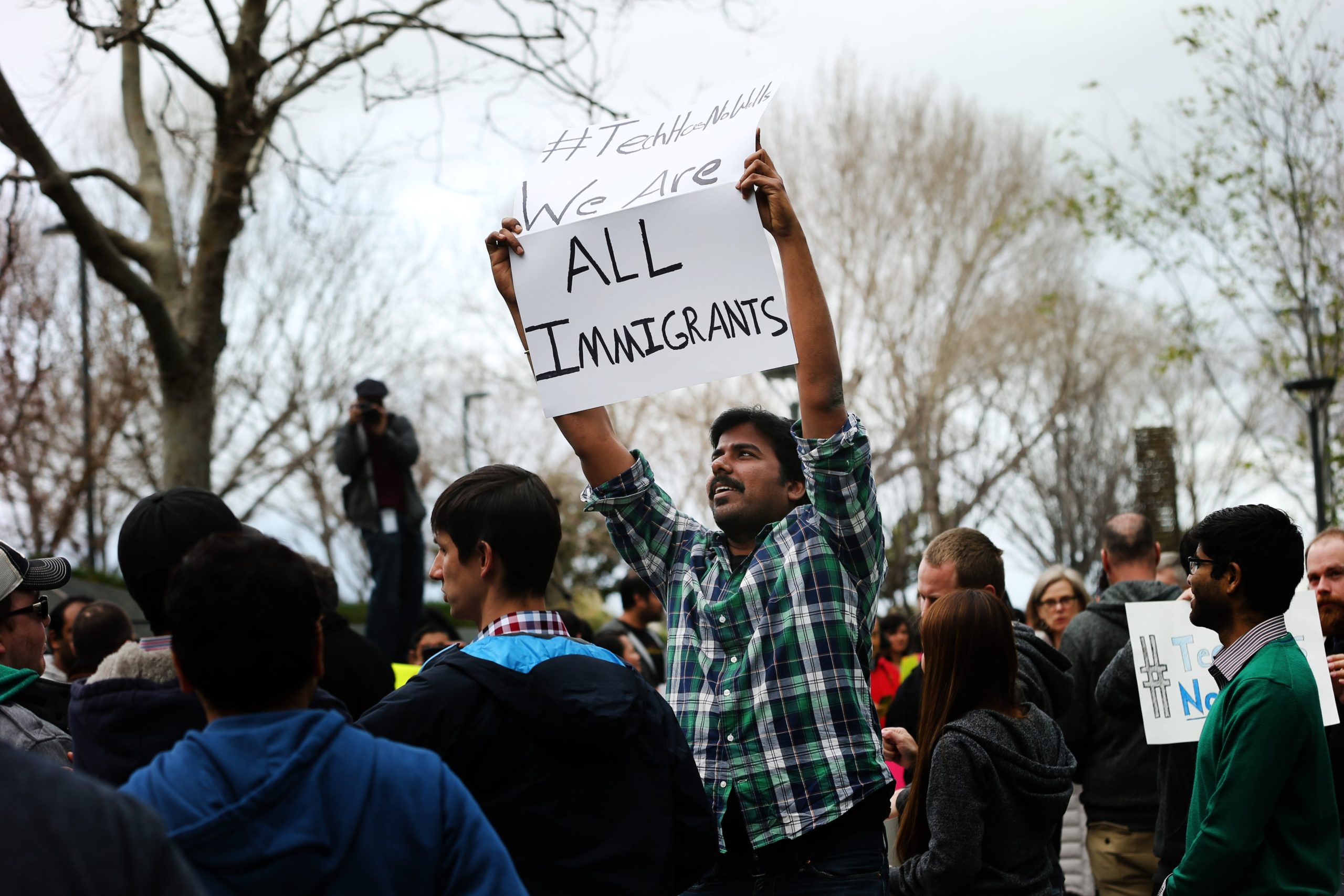 A man holds up a sign in the middle of a protest crowd. The sign reads 