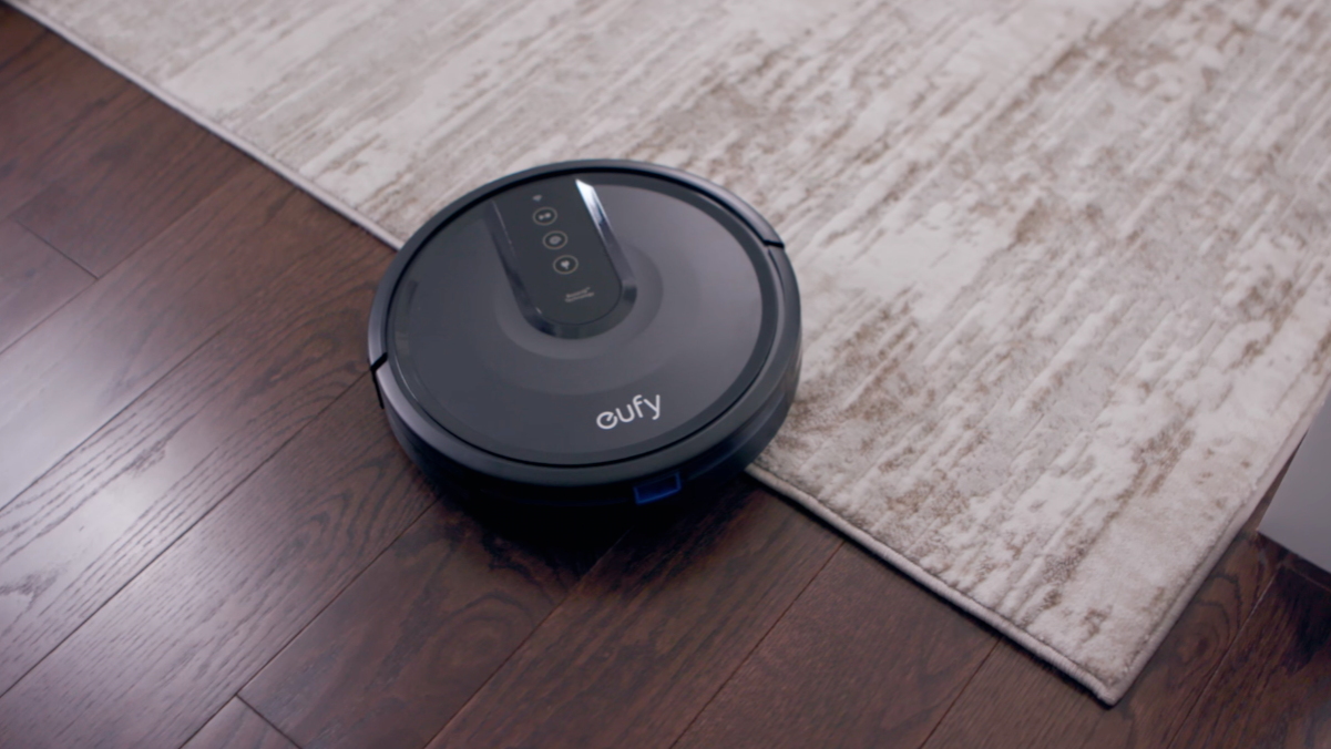 Black eufy robot vacuum against wooden floor and beige carpet