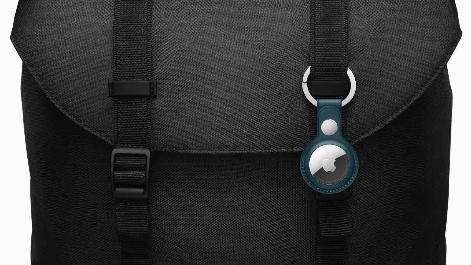 a close-up of an apple airtag in a blue case affixed to a black backpack