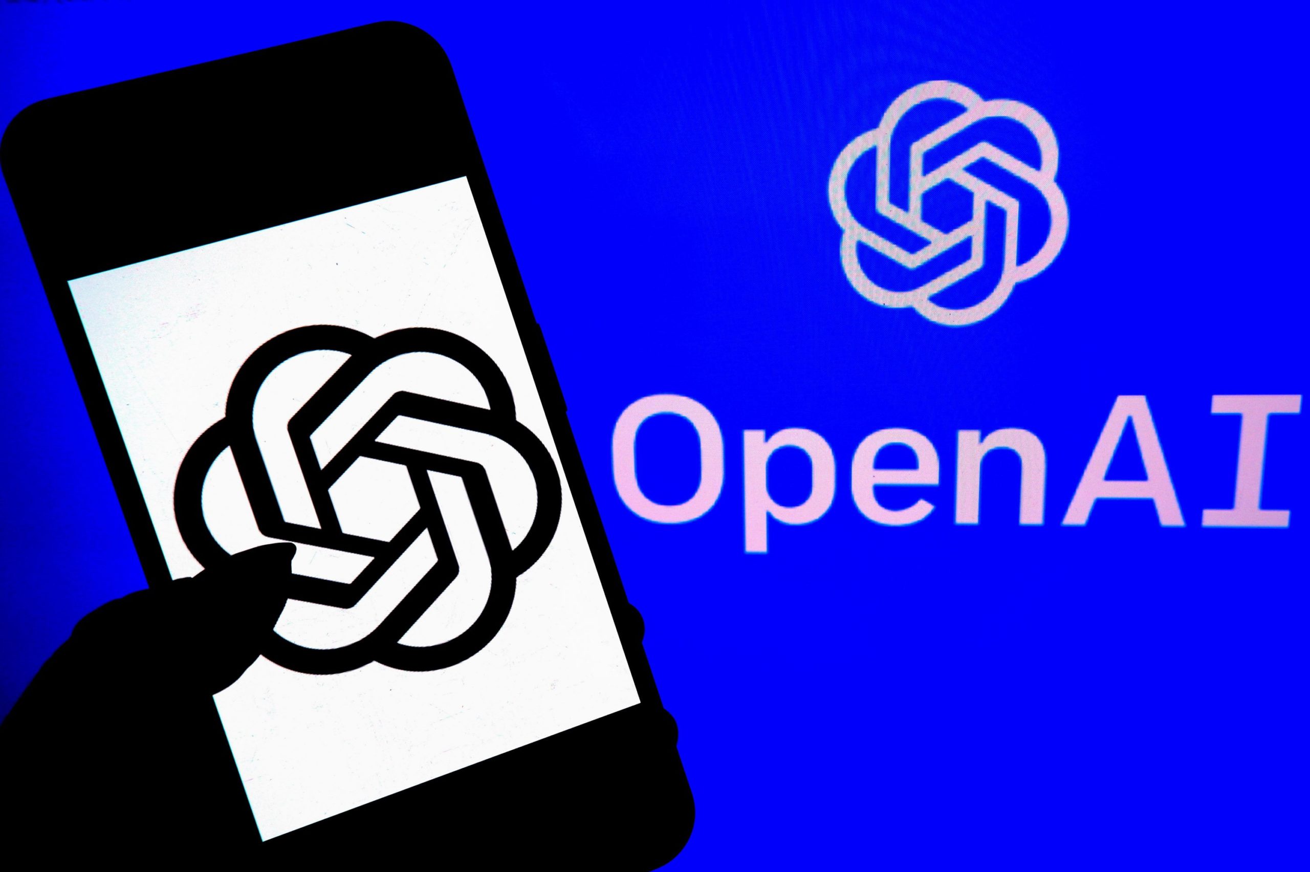 A hand holding a smartphone with the OpenAI symbol in front of the OpenAI logo