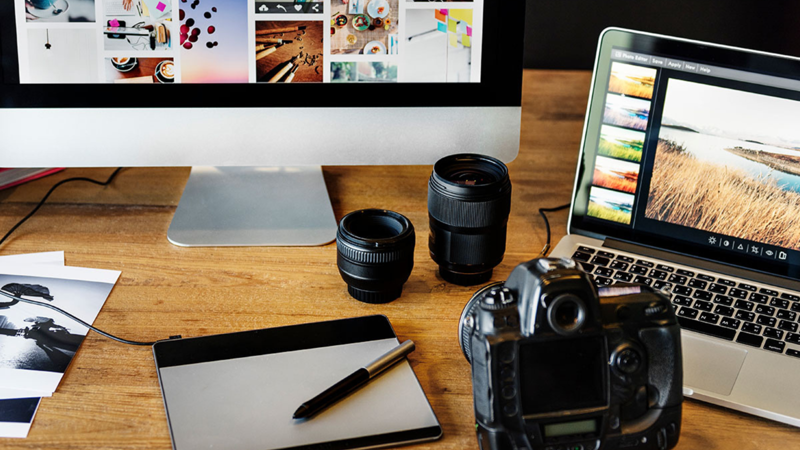 desktop computer next to laptop, camera, camera lenses, and more