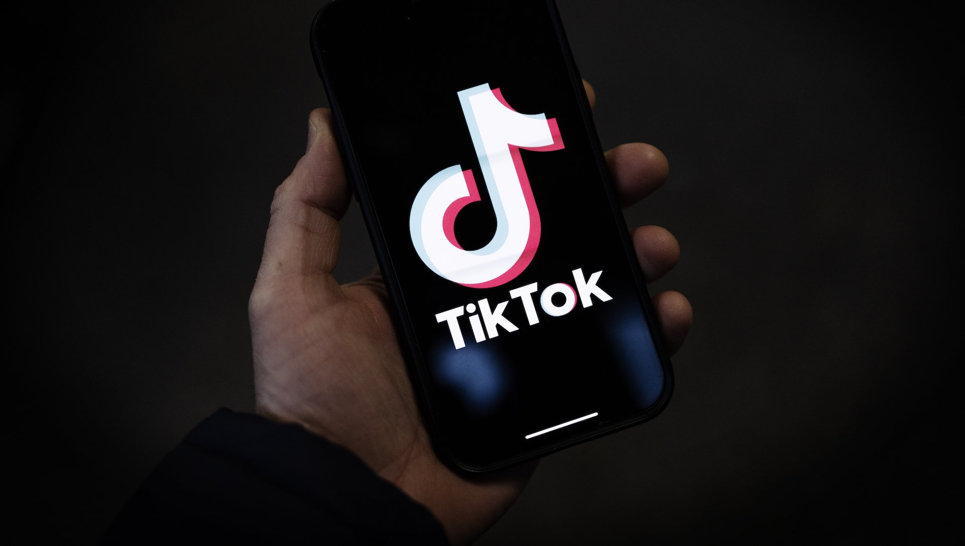 A hand holds a smartphone showing the TikTok logo.