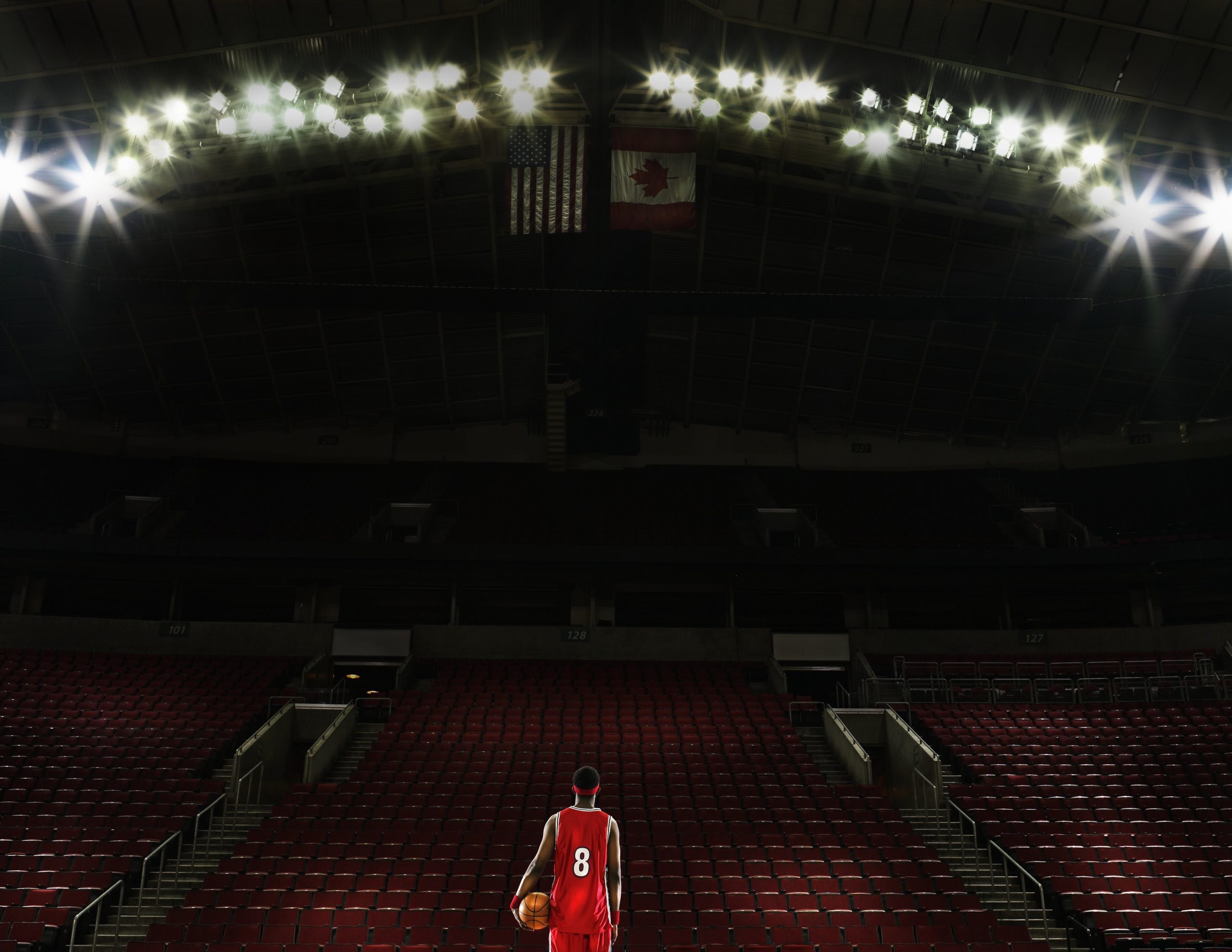 Basketball player standing on court holding basketball, rear view 