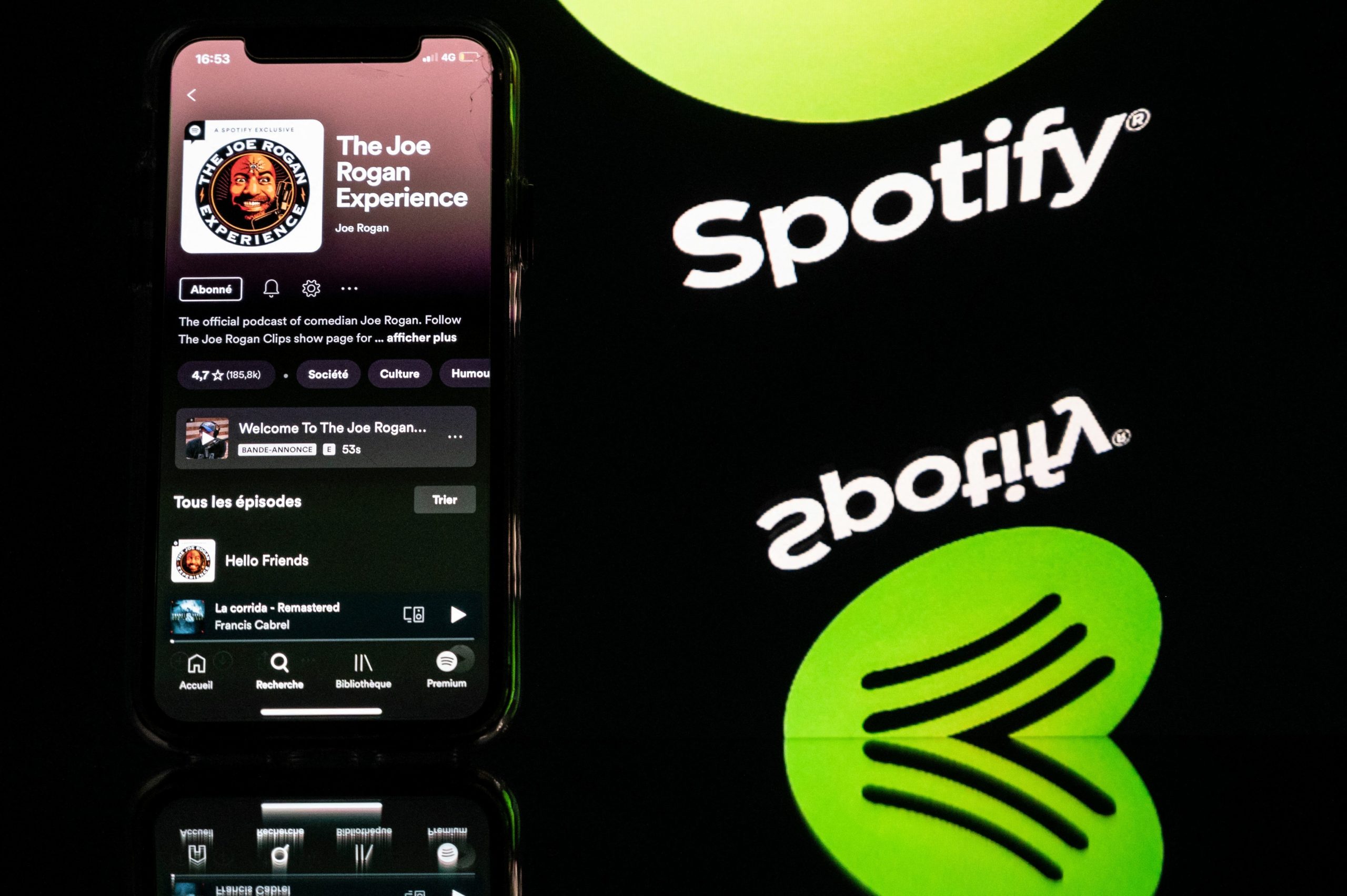 A smartphone displaying the Joe Rogan podcast and a screen displaying the Spotify's logo
