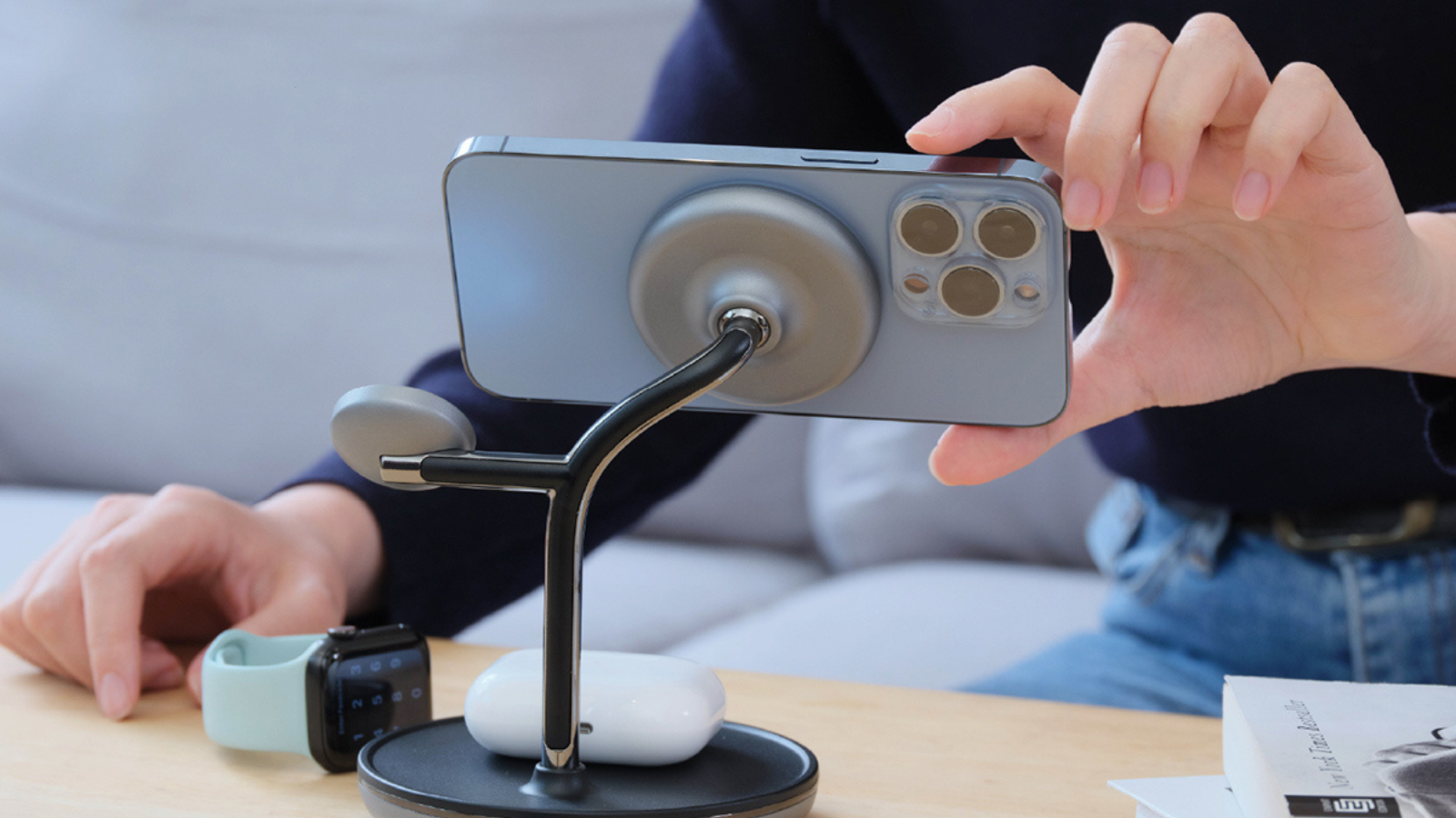 close up of person's hands attaching phone to omnia m3+ chaging station on desk with airpods, and apple watch