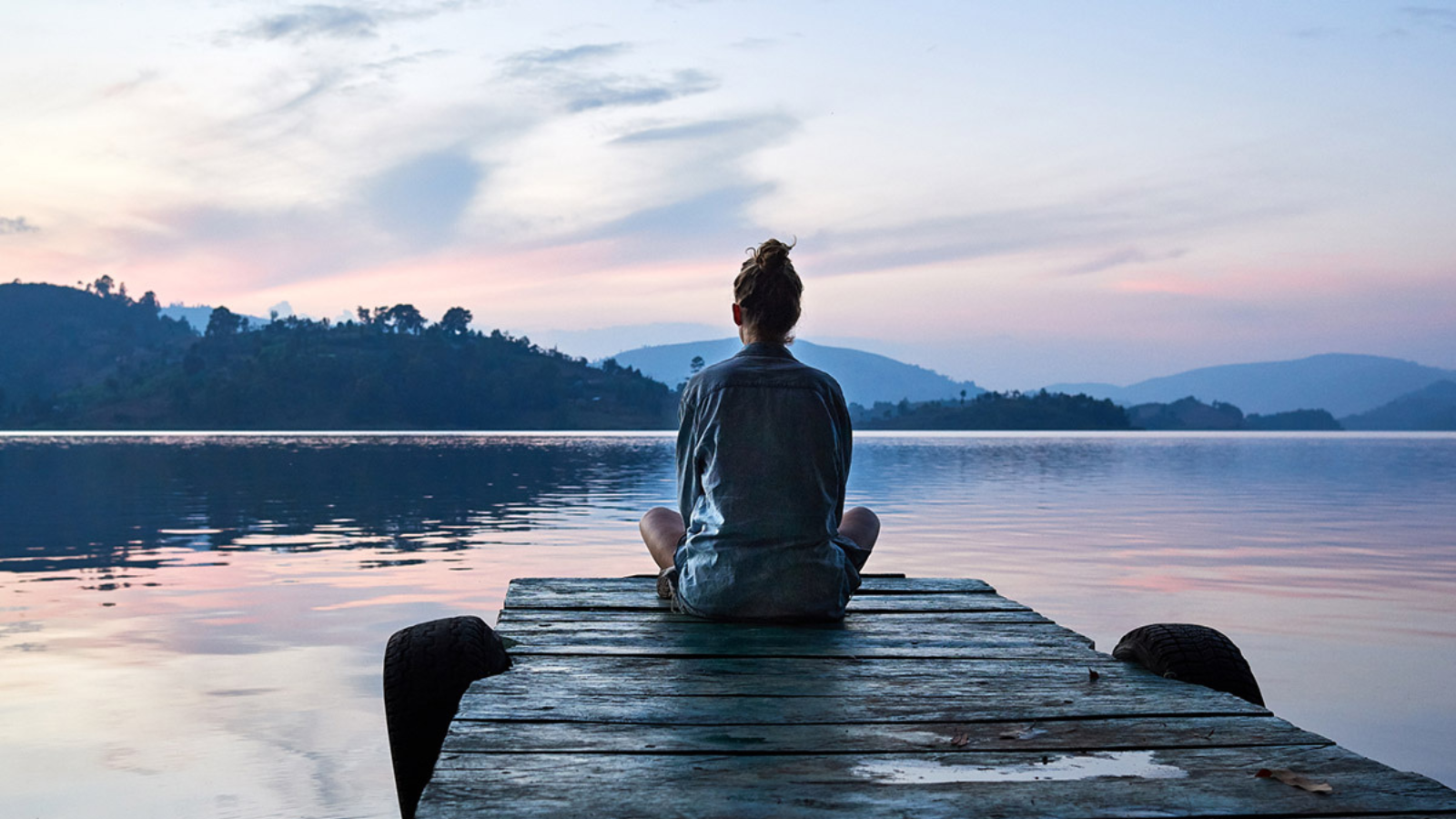 woman sitting on dock meditating with sunset in background