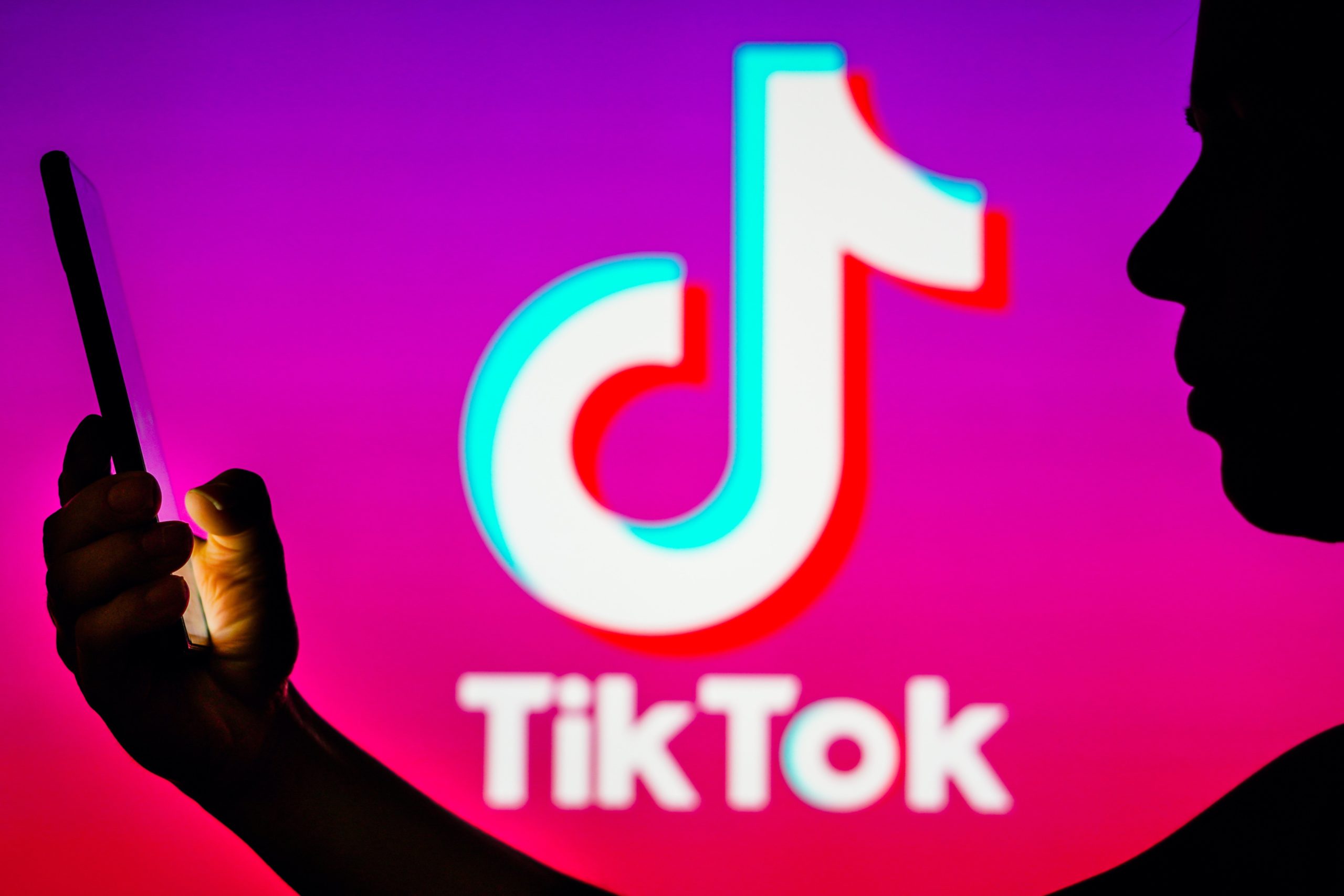 In this photo illustration, a person's silhouette holds a smartphone with the TikTok logo in the background. 