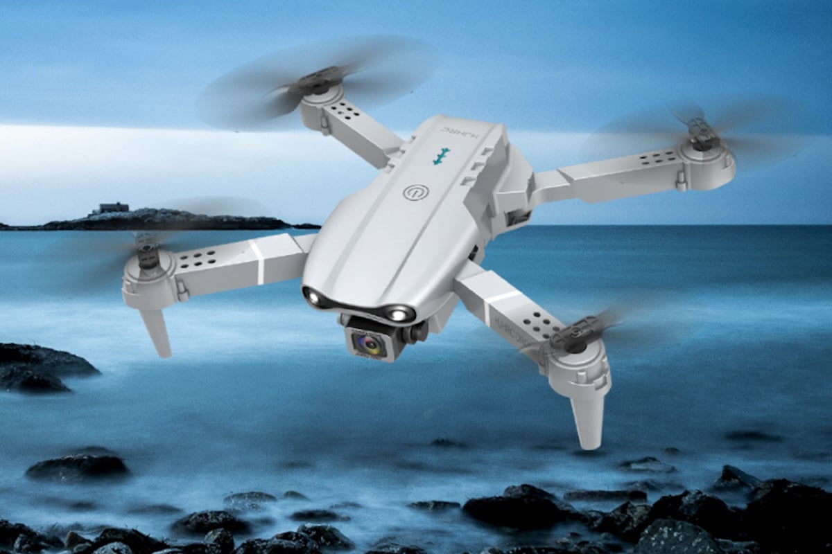 stock art of a camera drone flying across a dark blue sky, and over a body of water and cliffs