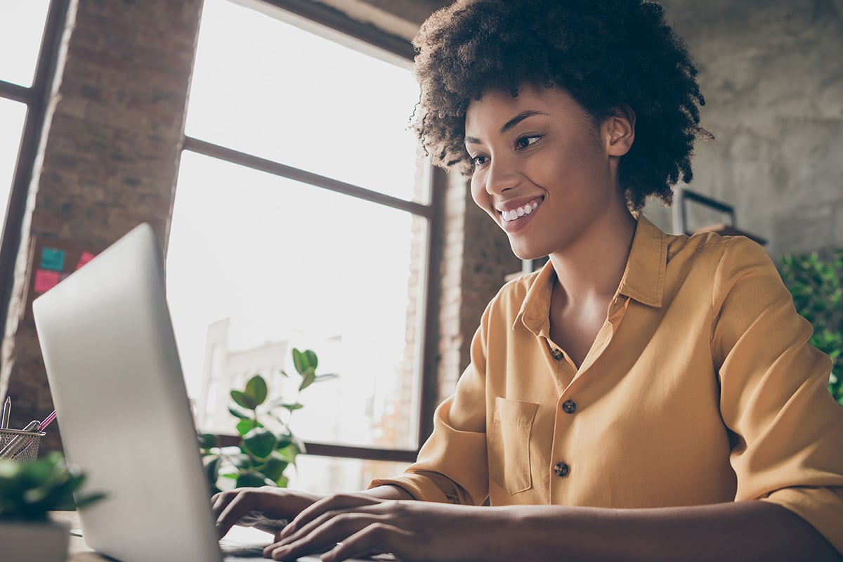 girl is sitting at a laptop smiling at the screen, her hands are on the keyboard