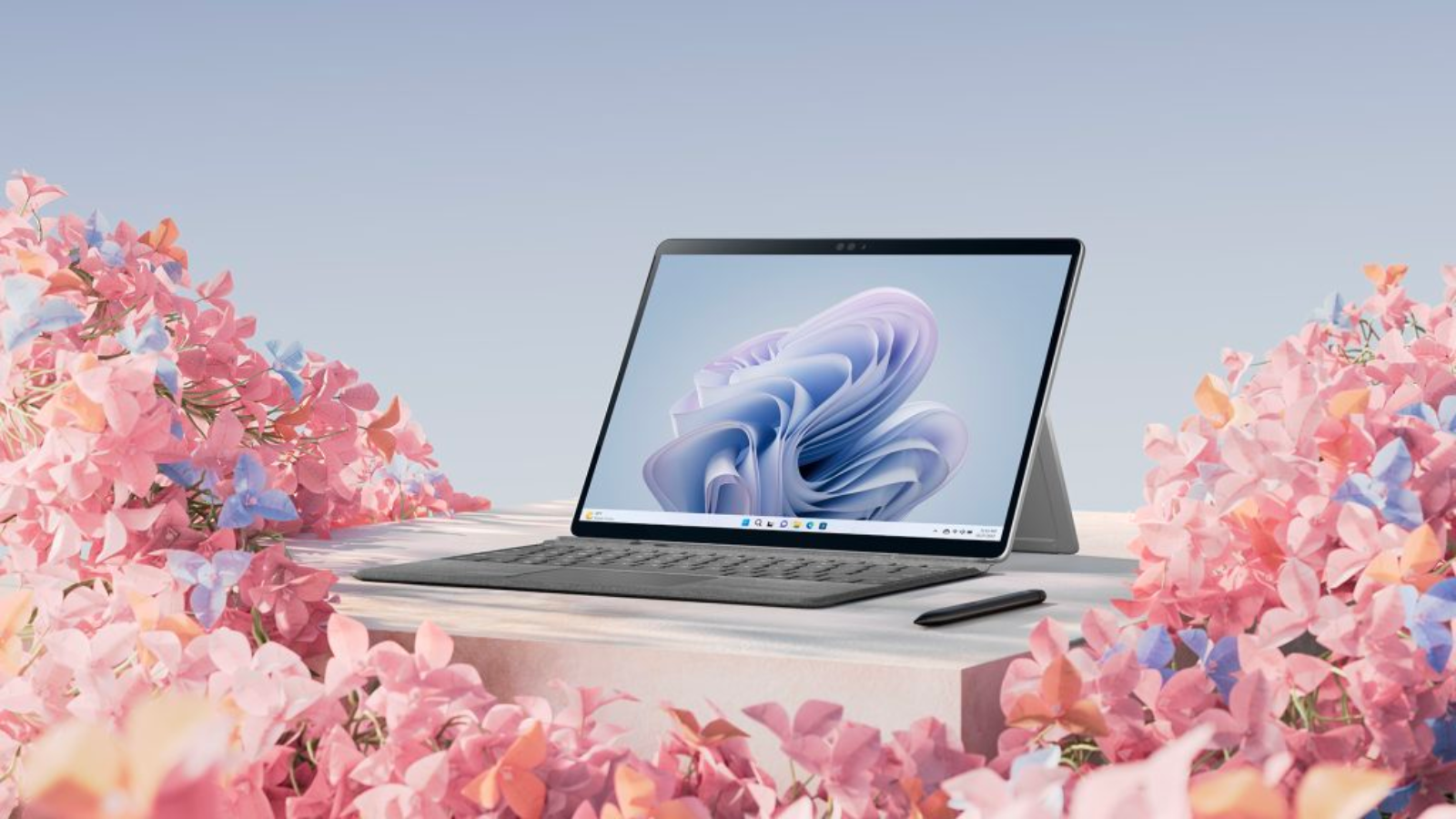 the microsoft surface pro 9 with a keyboard and a pen on a cream-colored surface amid beds of pink flowers