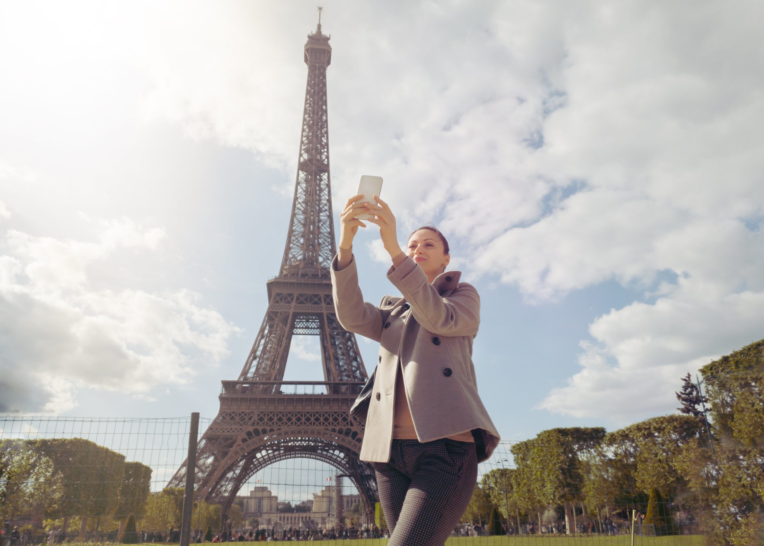 Female solo traveler make photo of Eiffel tower with smartphone while sightseeing in Paris