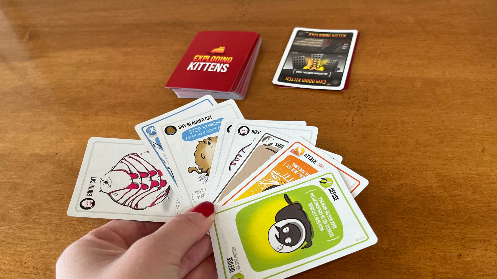 Manicured hand holding exploding kittens cards