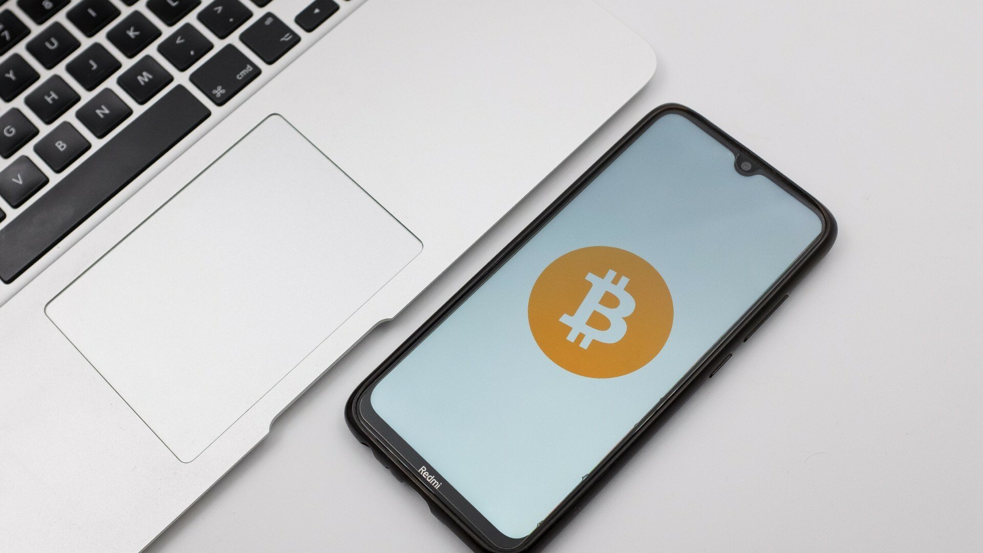 Bitcoin logo appears on smartphone sitting on a desk beside a keyboard.