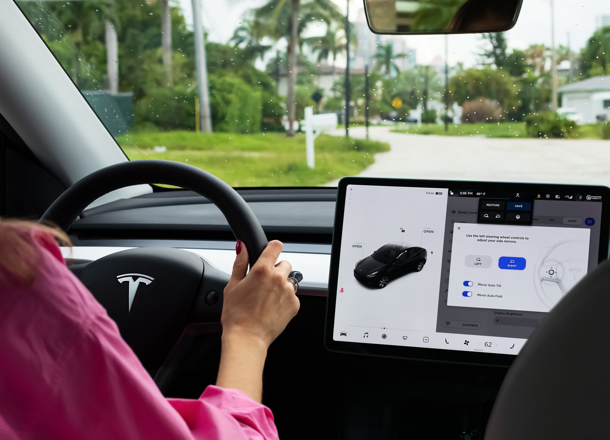 Woman's hands at the steering wheel of a Tesla showing its LCD touch screen