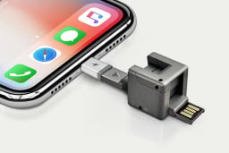 gray one inch cube with iphone charger, usb stick, and other adapters are against a white background, plugged into an iphone charging socket