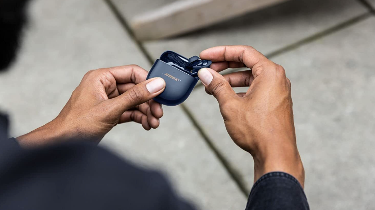 A pair of hands holding the Bose earbuds, pavement in the background