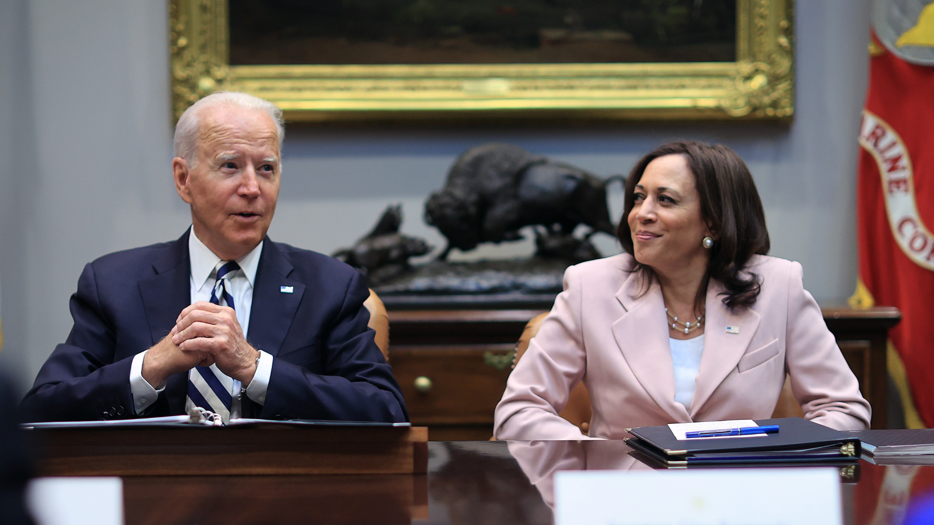 Biden and Harris sit side by side at a table. She is in a light pink suit jacket and he is in a tie and navy blazer