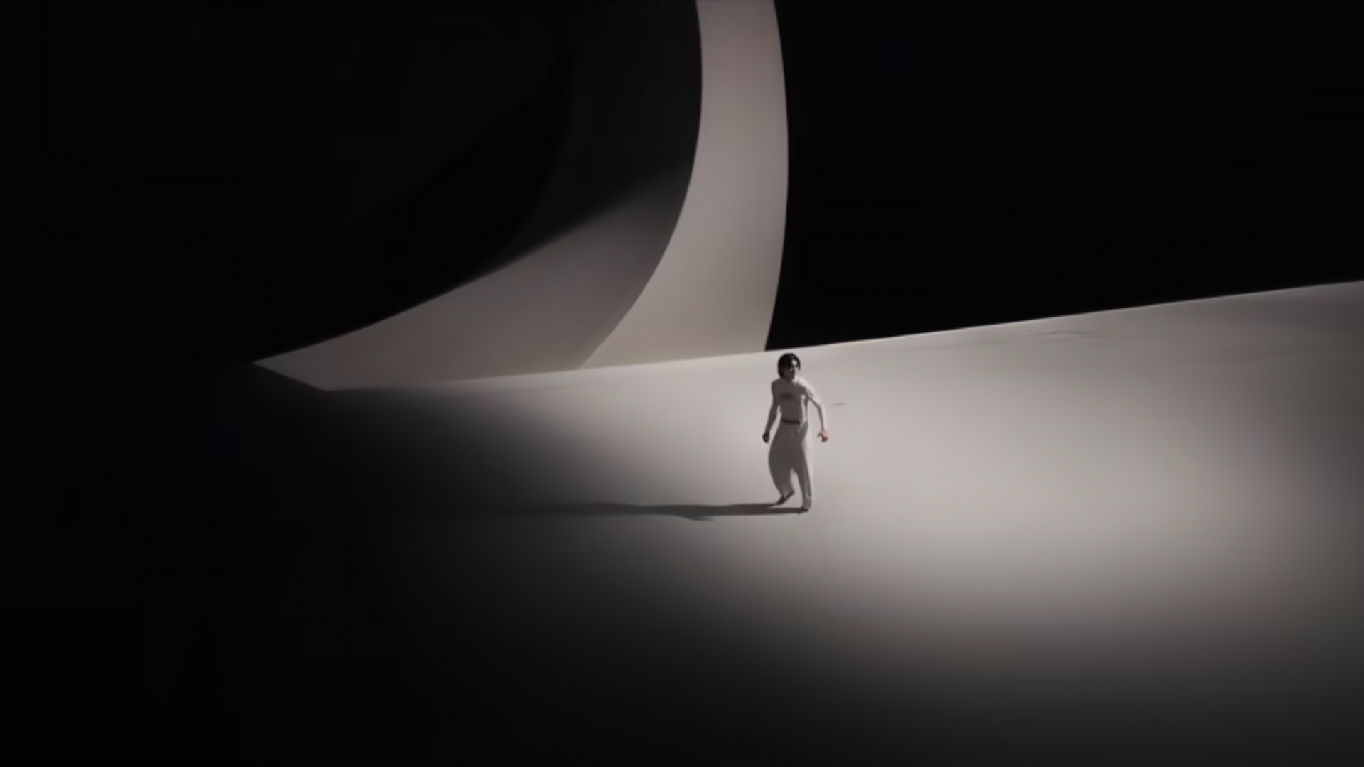 A screenshot from the Masquerade music video. Lee stands in the middle of a dark expanse, dressed in white.