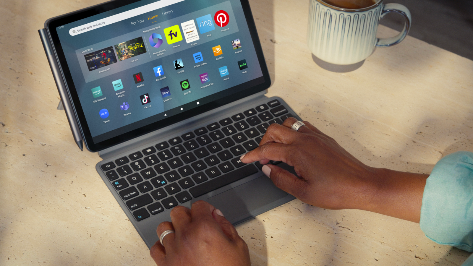 a close-up of a woman typing on an amazon fire 11 max tablet with a keyboard case and stylus attached