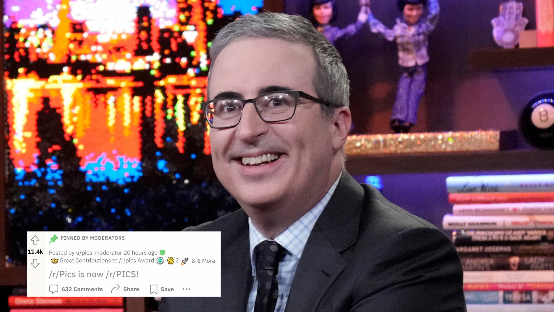A man with glasses sits on a talk show grinning.