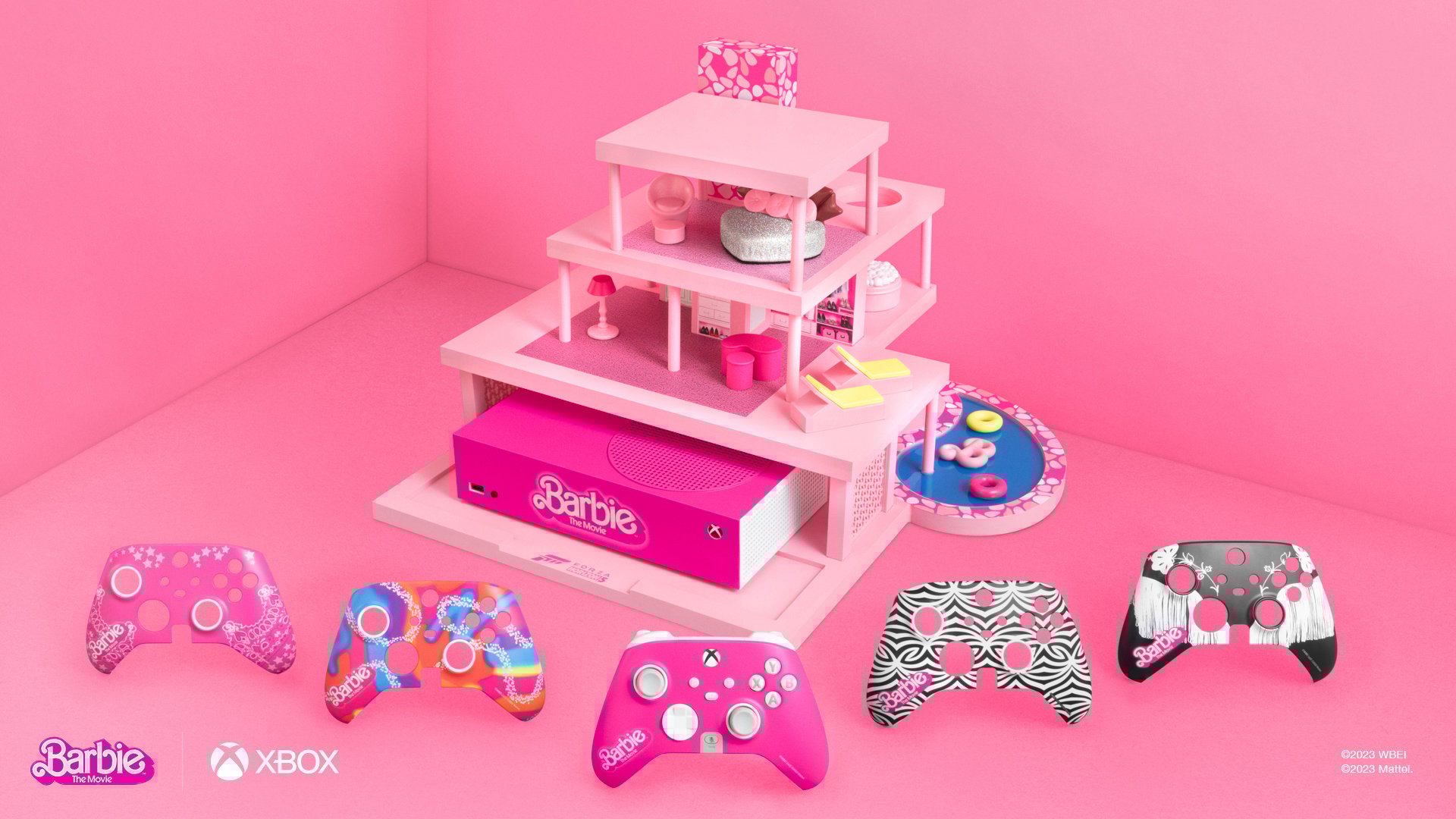 A product photo of the 5 new Barbie XBox controller skins in the foreground. In the background, a Barbie-themed xbox (bright pink, with the Barbie logo) housed in a mini version of Barbie's dream house, complete with pool.