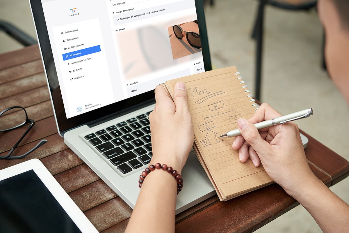 Someone's hands shown writing in a notepad in front of an open laptop.