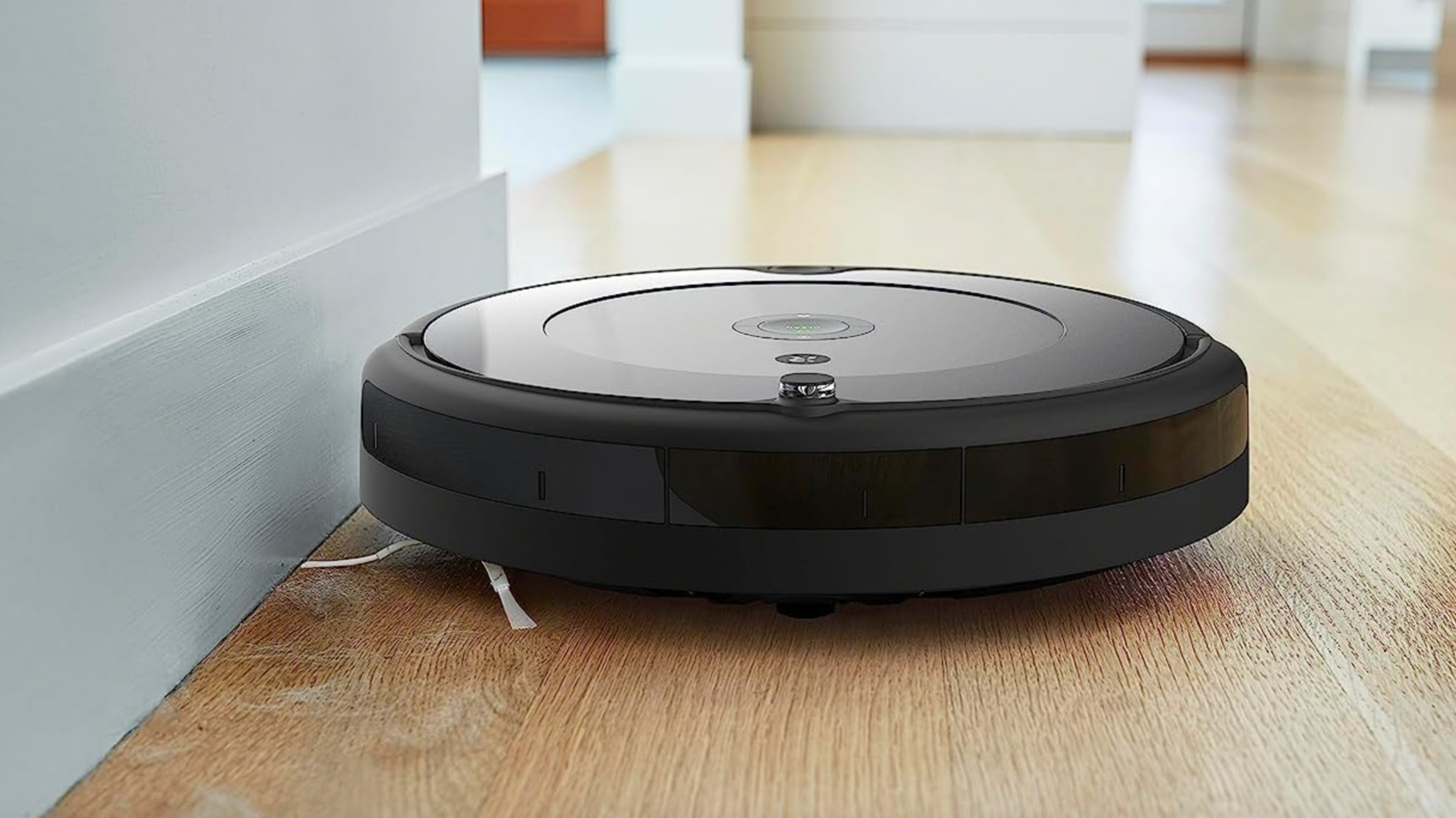 Roomba cleaning along the edge of a wall on a wooden floor